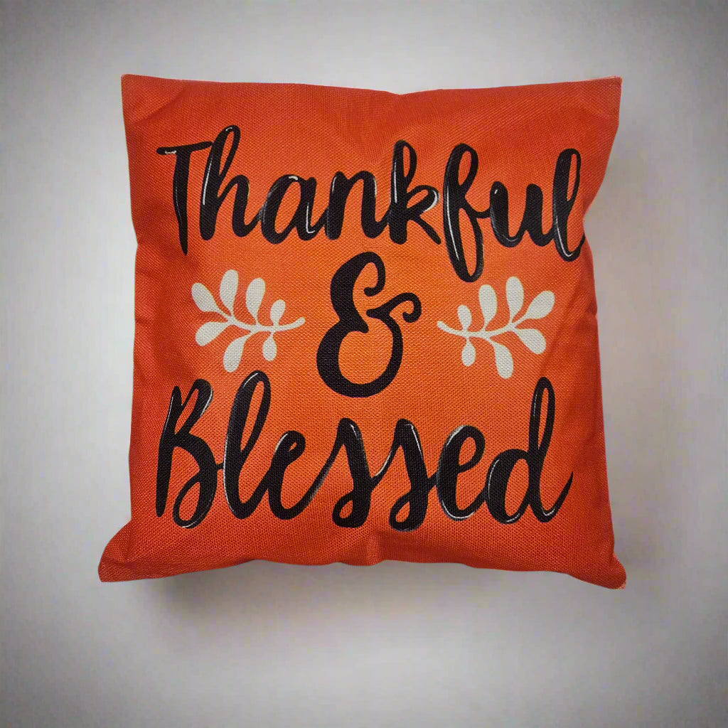 Orange pillow with 'Thankful & Blessed' text on a white surface